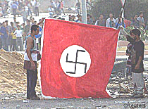 October 6, 2000: Palestinians hold up flag with a Nazi swastika in front of an Israeli army outpost at the Netzarim junction, Gaza Strip, in support of the Nazi goal of genocide against the Jewish people.